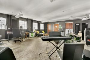 Studio room with drums, amps, keyboard, PA, lounge area, desk, studio monitors, and sound panels.